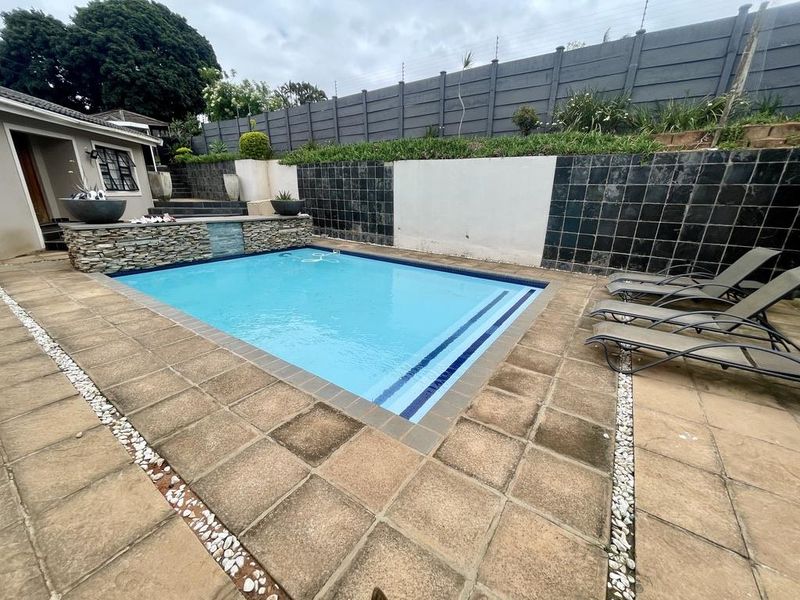 Outdoor pool area featuring a swimming pool with stone cladding detail, surrounded by paved decking and enclosed by a high boundary wall with electric fencing.