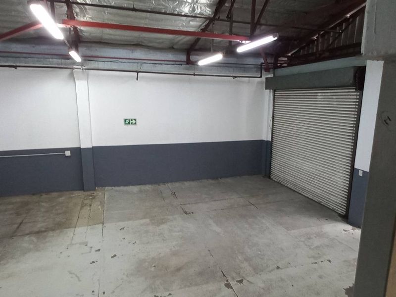 Spacious industrial garage featuring a roller shutter door, exposed ceiling structure, and durable concrete flooring, suitable for storage or workshop use.