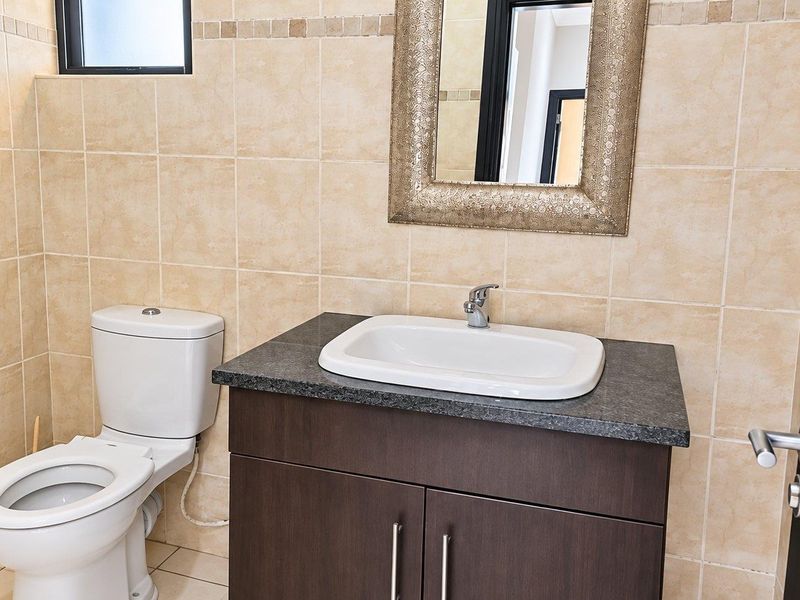 A clean, well-maintained bathroom featuring a modern vanity with a granite countertop, ceramic basin, and neutral wall tiling.