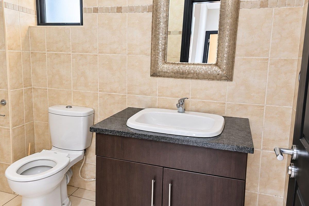A clean, well-maintained bathroom featuring a modern vanity with a granite countertop, ceramic basin, and neutral wall tiling.