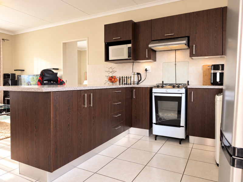 A functional kitchen featuring dark wood cabinetry, laminate countertops, a freestanding oven with extractor fan, and tiled flooring.