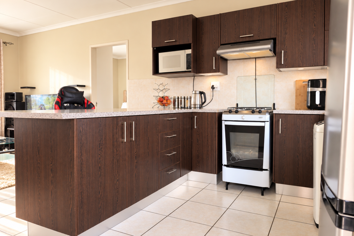 A functional kitchen featuring dark wood cabinetry, laminate countertops, a freestanding oven with extractor fan, and tiled flooring.