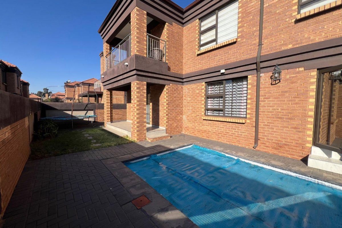 Rear exterior view of the townhouse featuring a paved patio area, a swimming pool with a cover, and a balcony overlooking the garden.