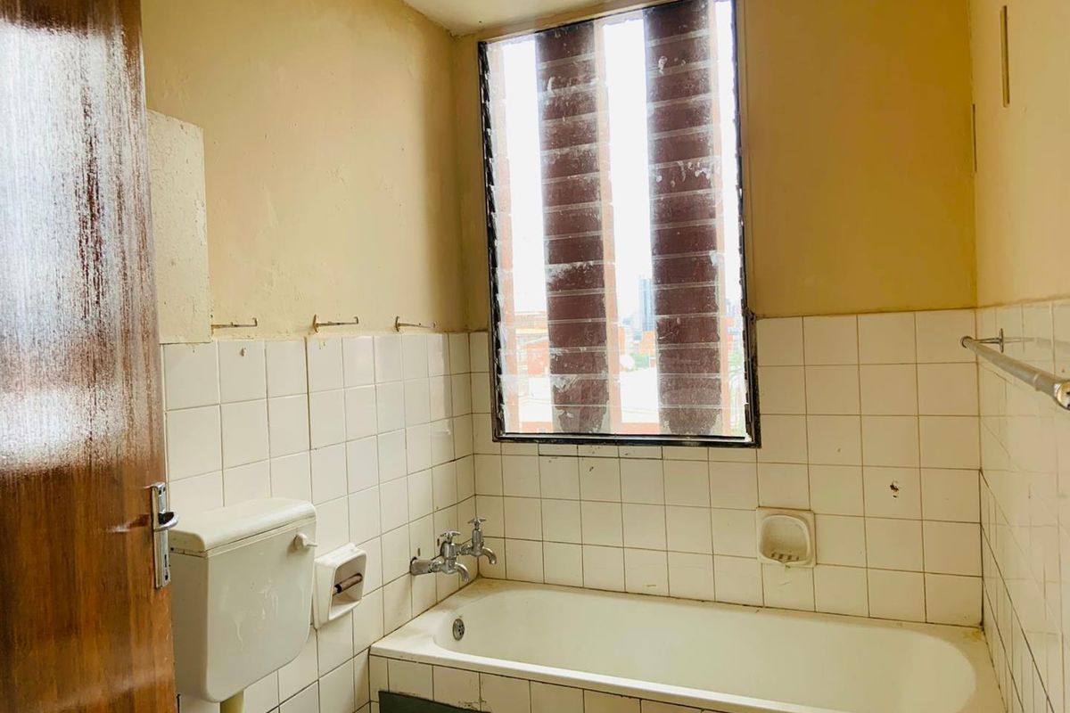 A dated bathroom featuring a standard bathtub, wall-mounted toilet cistern, and tiled walls, requiring significant renovation and cosmetic updates.
