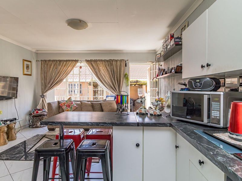 Open-plan living and kitchen area featuring tiled flooring, kitchen cabinetry with laminate countertops, and a breakfast bar leading to an outdoor patio.