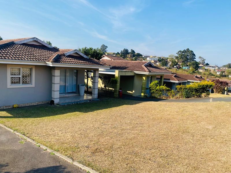 Front view of a townhouse complex featuring tiled roofs, covered patio areas, and a shared lawn space with paved driveway access.