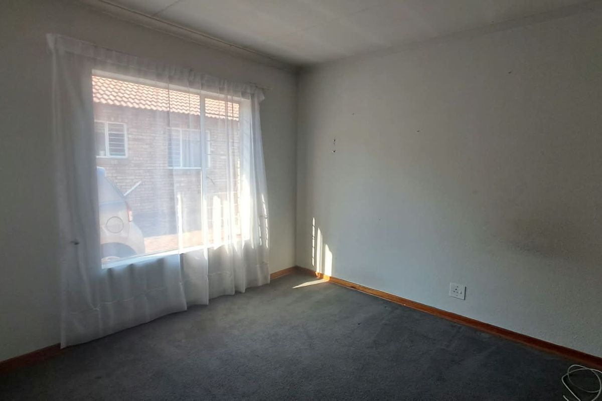 An empty bedroom featuring carpeted flooring and a large window, providing a blank canvas for personalization.