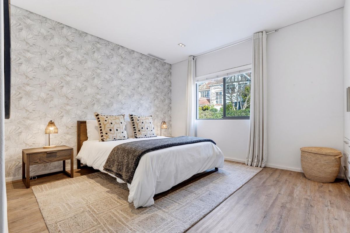 A well-maintained bedroom featuring modern laminate flooring, recessed lighting, and a large window with neutral curtains.