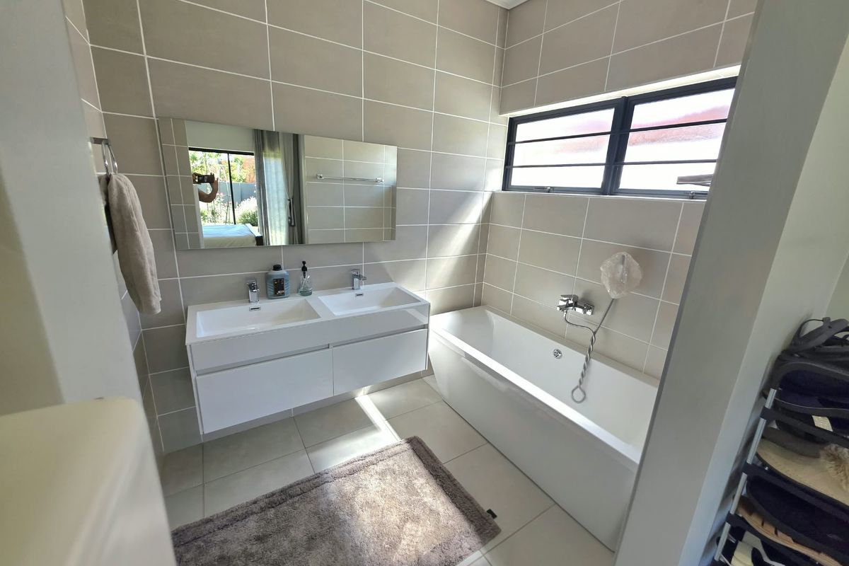 Modern bathroom featuring a double vanity with wall-mounted mirror, a built-in bathtub, and neutral floor-to-ceiling wall tiles.