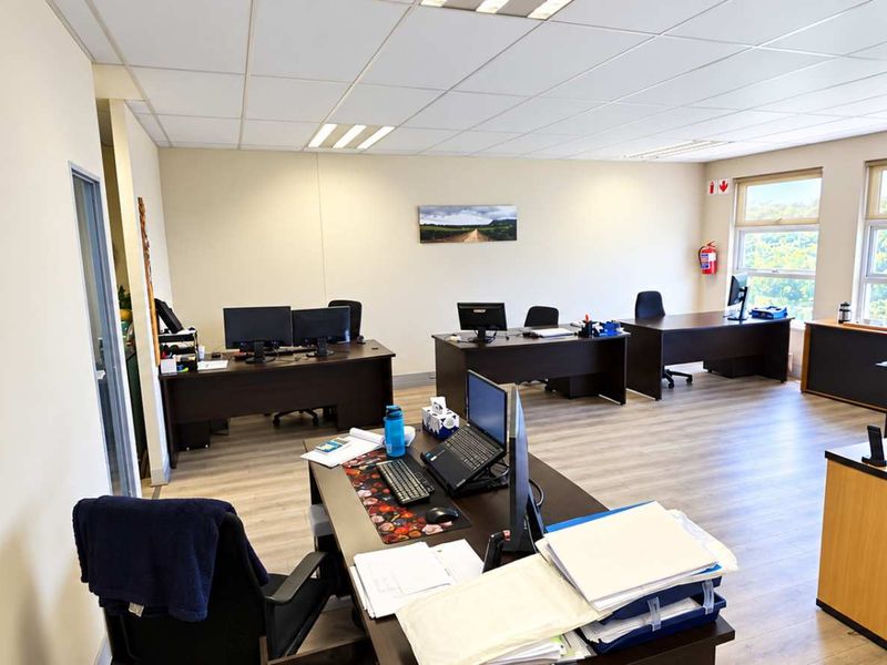 A spacious, well-lit open-plan office area featuring laminate flooring, suspended ceilings, and large windows providing natural light.
