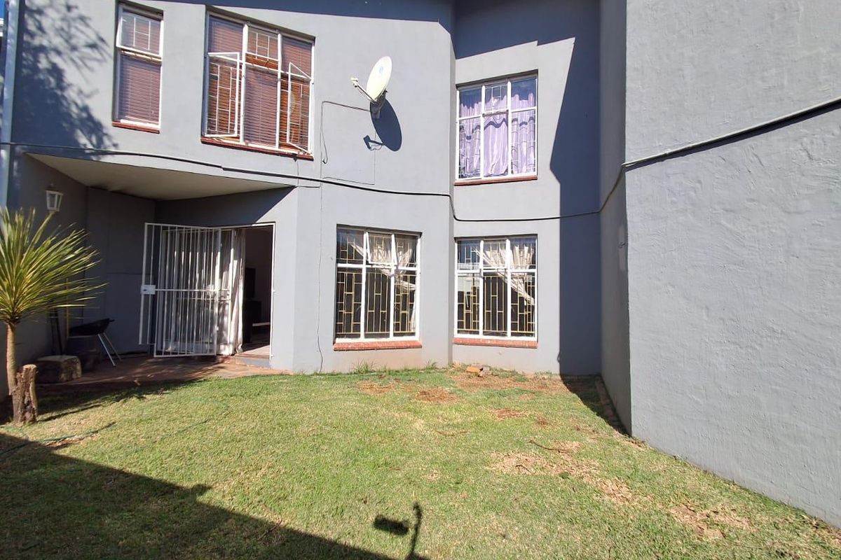 Rear view of the townhouse featuring a private garden area, paved patio section, and multiple windows with security bars.