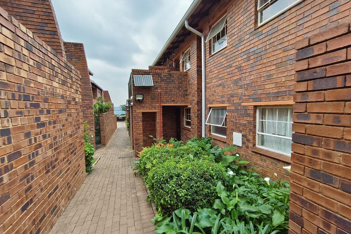 A view of the exterior rear walkway featuring face brick construction, paved pathways, and established garden beds along the apartment building.