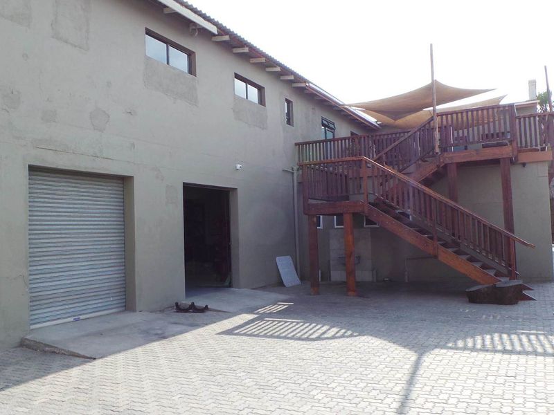 Rear exterior view of the retail property featuring a paved yard, roller shutter door, and an elevated timber deck with staircase access.