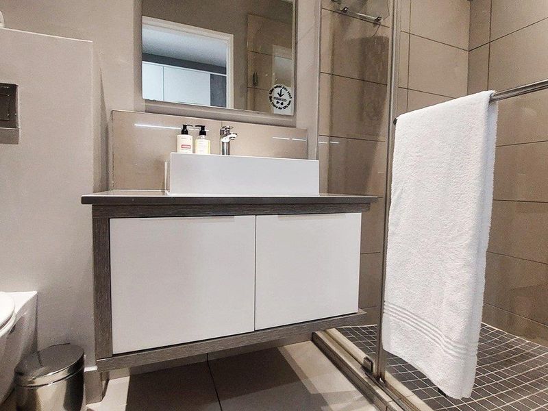 Modern bathroom featuring a wall-mounted vanity with vessel sink, glass-enclosed shower with tiled flooring, and a wall-mounted toilet.