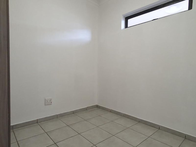 A clean, empty bedroom featuring neutral tiled flooring, a built-in cupboard, and a high-level window providing natural light.