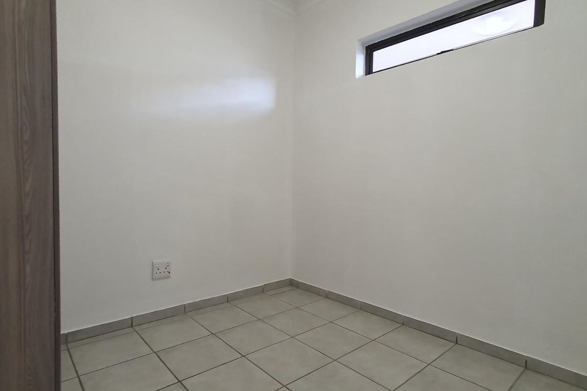A clean, empty bedroom featuring neutral tiled flooring, a built-in cupboard, and a high-level window providing natural light.