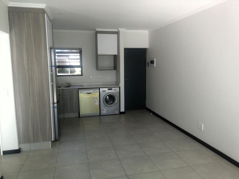 A clean, modern kitchen area featuring tiled flooring, built-in cabinetry, and dedicated plumbing connections for laundry appliances.