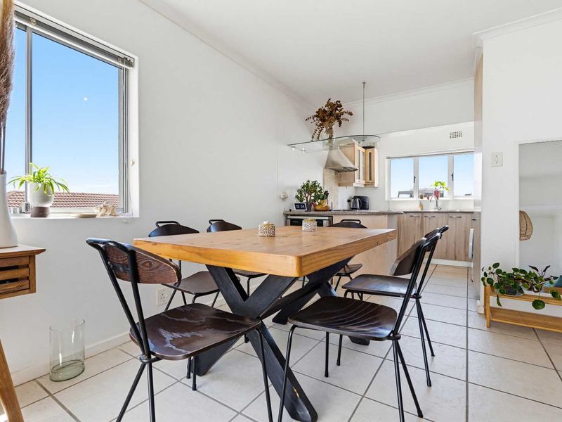 An open-plan living and dining area featuring tiled flooring, a functional kitchen with cabinetry, and natural light from large windows.