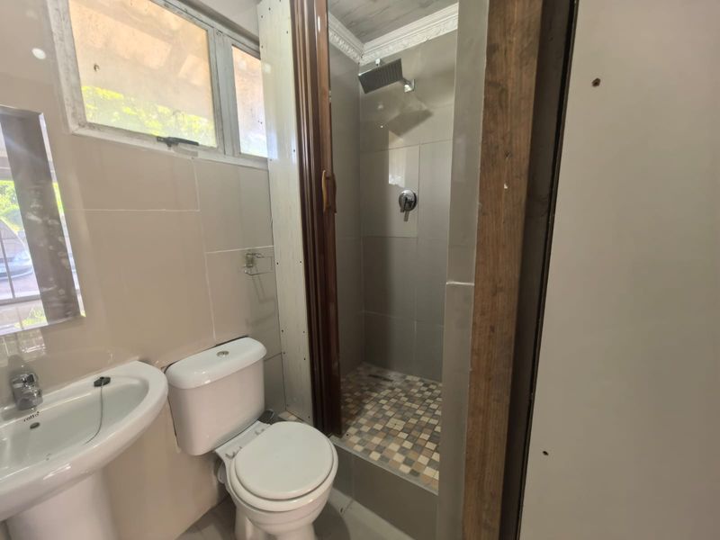A compact bathroom featuring a pedestal basin, toilet, and a tiled shower enclosure. The space requires finishing touches to the wall paneling and door frame.