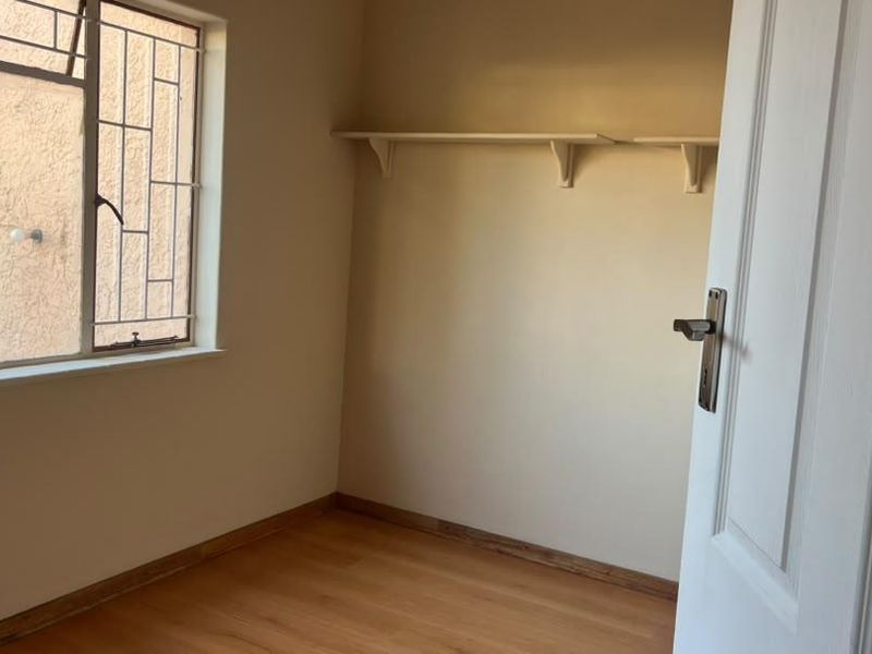 An empty bedroom featuring laminate flooring, built-in wall shelving, and security bars on the window.
