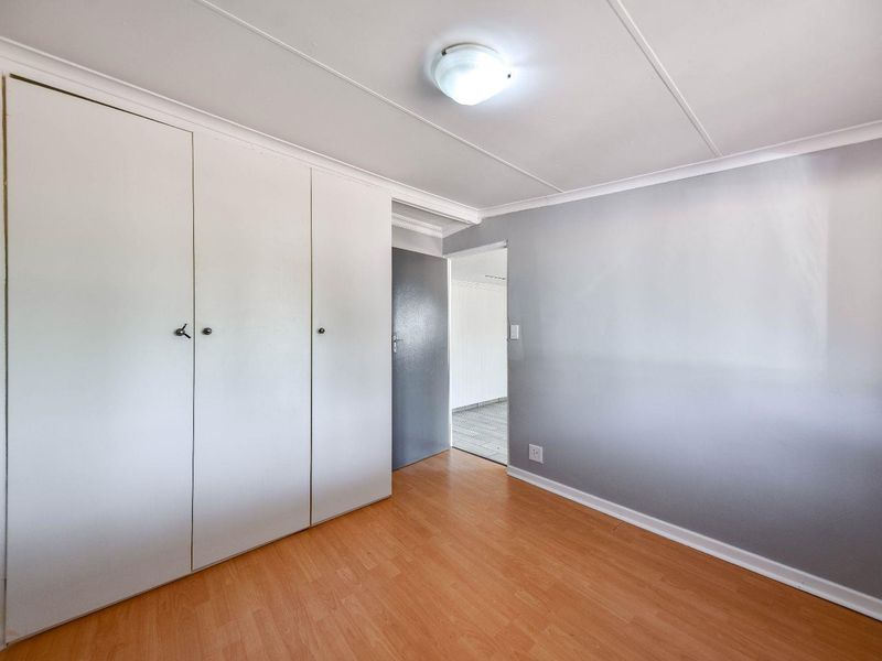 A clean, empty bedroom featuring light-toned laminate flooring, built-in cupboards, and neutral grey wall finishes.