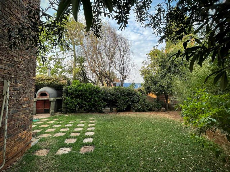 A private garden featuring a built-in brick pizza oven, lush greenery, and a stone paver pathway leading through the lawn.