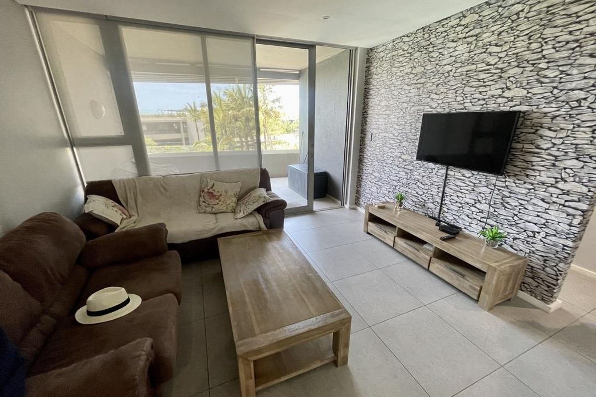 A bright living room featuring large sliding glass doors leading to a balcony, tiled flooring, and a decorative stone-effect feature wall.