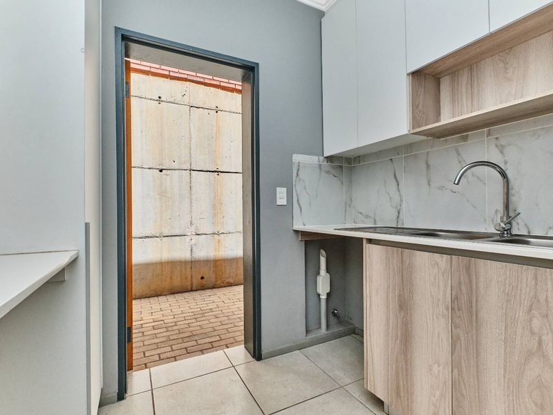 A clean and modern scullery featuring built-in cabinetry, marble-look splashback, stainless steel sink, and direct access to an outdoor paved area.