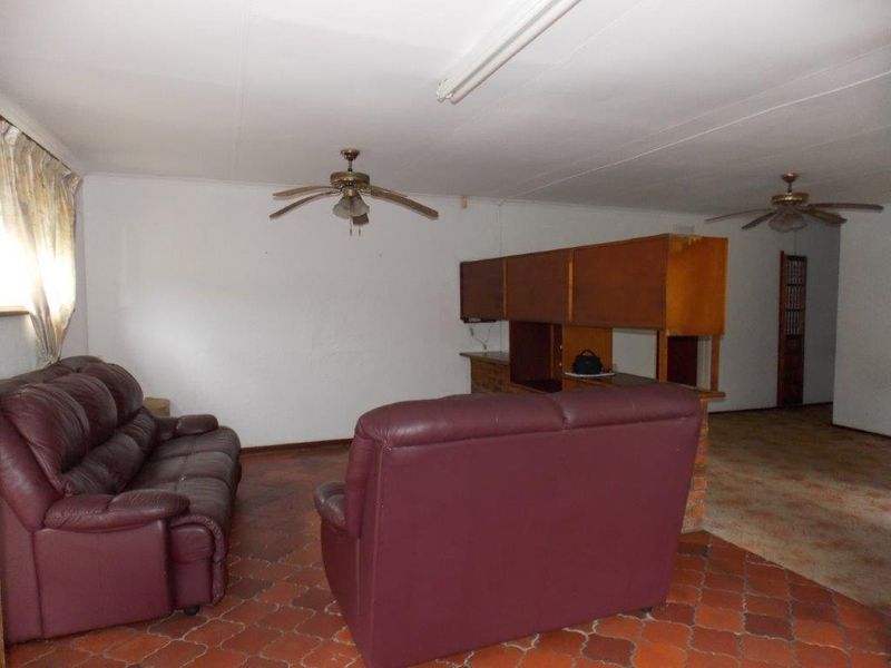 A dated living area featuring terracotta tile flooring, ceiling fans, and a built-in room divider, offering potential for modernization and renovation.