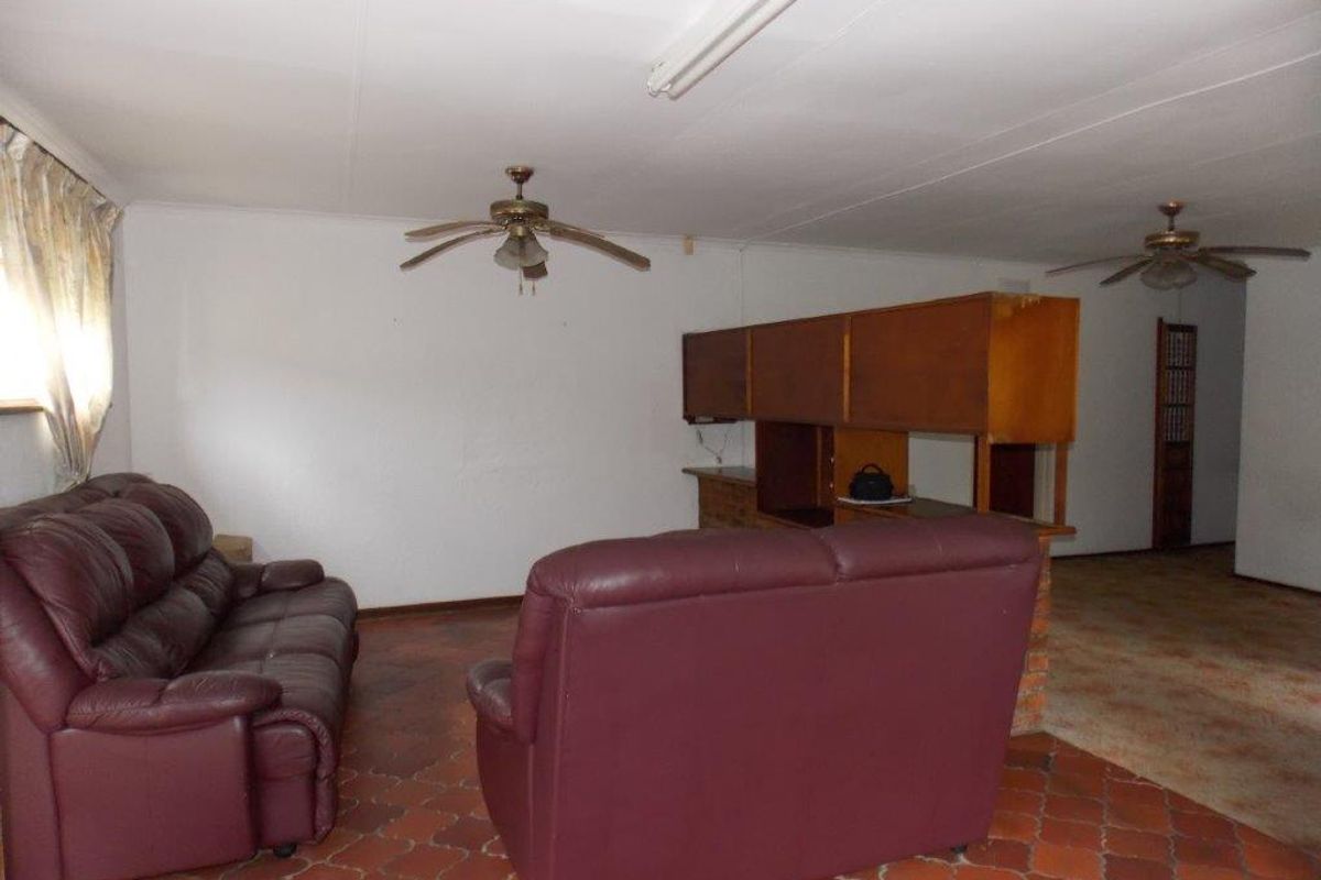 A dated living area featuring terracotta tile flooring, ceiling fans, and a built-in room divider, offering potential for modernization and renovation.