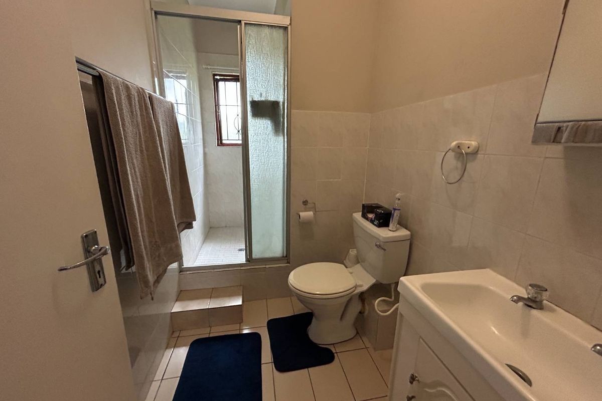 A functional bathroom featuring a shower cubicle, toilet, and vanity basin with tiled walls and flooring.