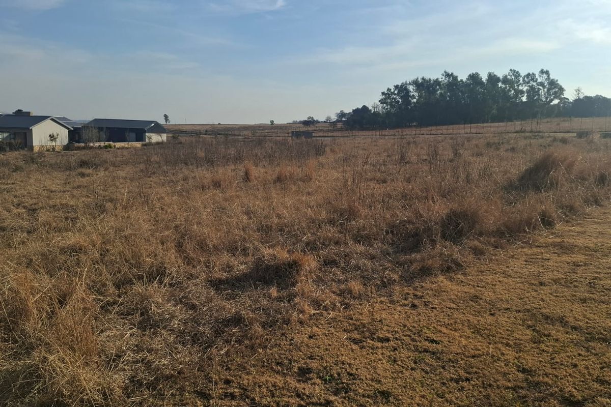 A wide-angle view of a vacant residential plot featuring dry grass and perimeter fencing, with neighboring properties visible in the distance.