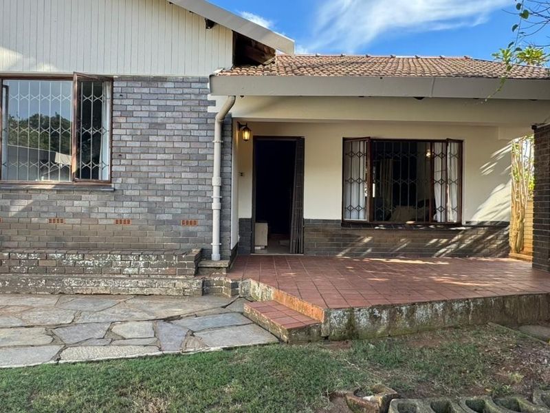 Rear exterior view of the house featuring a tiled patio, brick facade, and security-barred bay windows with stone paving in the garden area.