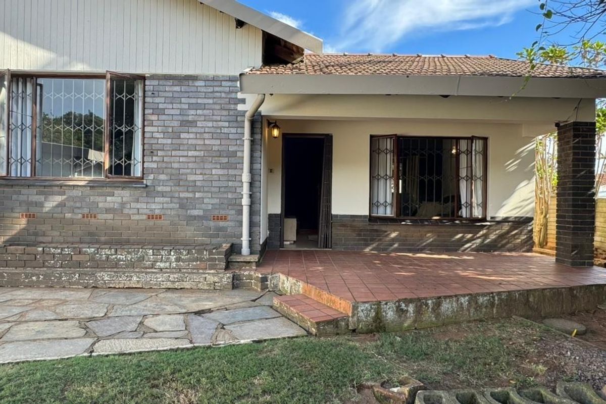 Rear exterior view of the house featuring a tiled patio, brick facade, and security-barred bay windows with stone paving in the garden area.