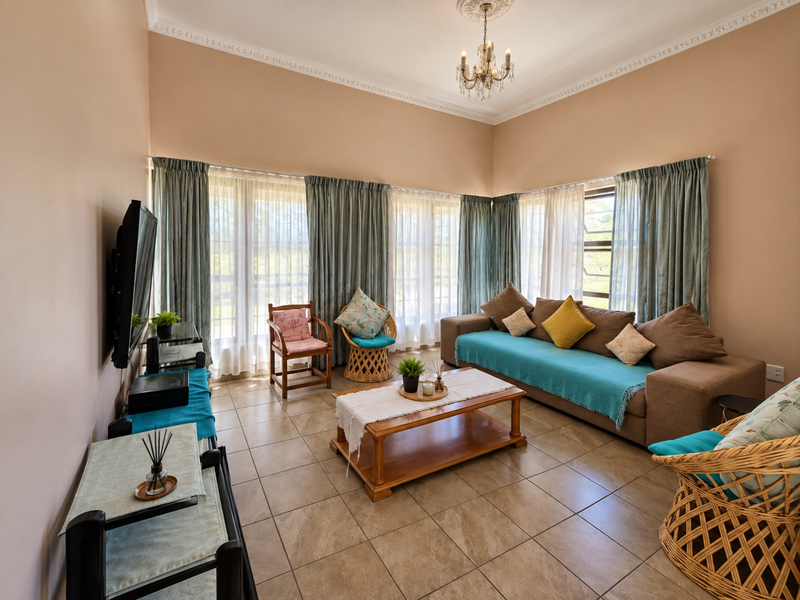 Spacious living room featuring tiled flooring, decorative ceiling cornice, a classic chandelier, and large windows allowing for ample natural light.