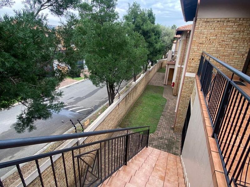 Exterior view of the apartment complex featuring a tiled staircase with metal railings, paved walkway, and perimeter wall with electric fencing.