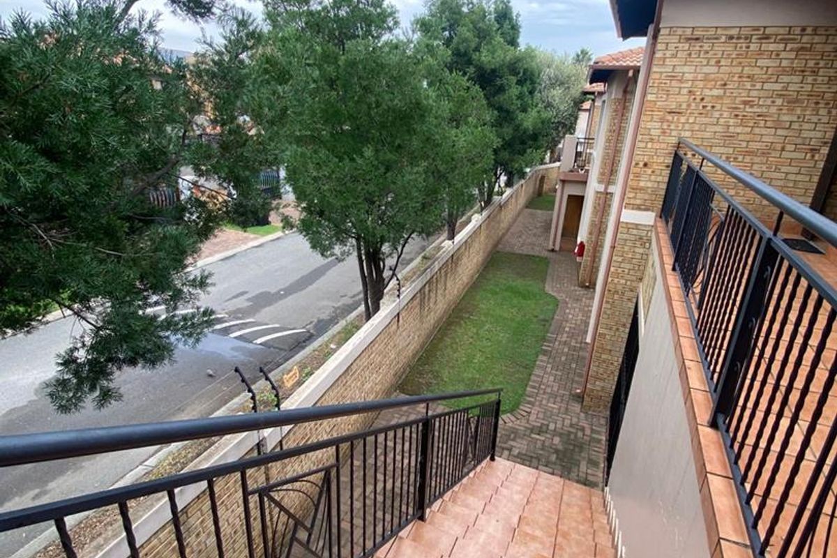 Exterior view of the apartment complex featuring a tiled staircase with metal railings, paved walkway, and perimeter wall with electric fencing.