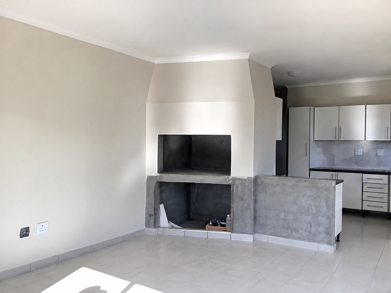 Open plan living area featuring a built-in fireplace and adjacent kitchen with white cabinetry and tiled flooring.