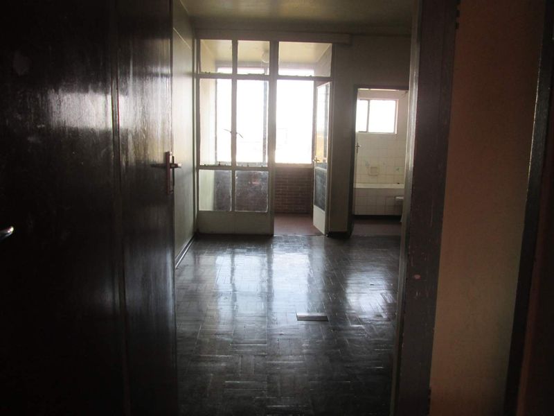 An empty living area featuring original parquet flooring and access to an adjoining balcony, showing signs of age and requiring cosmetic updates.