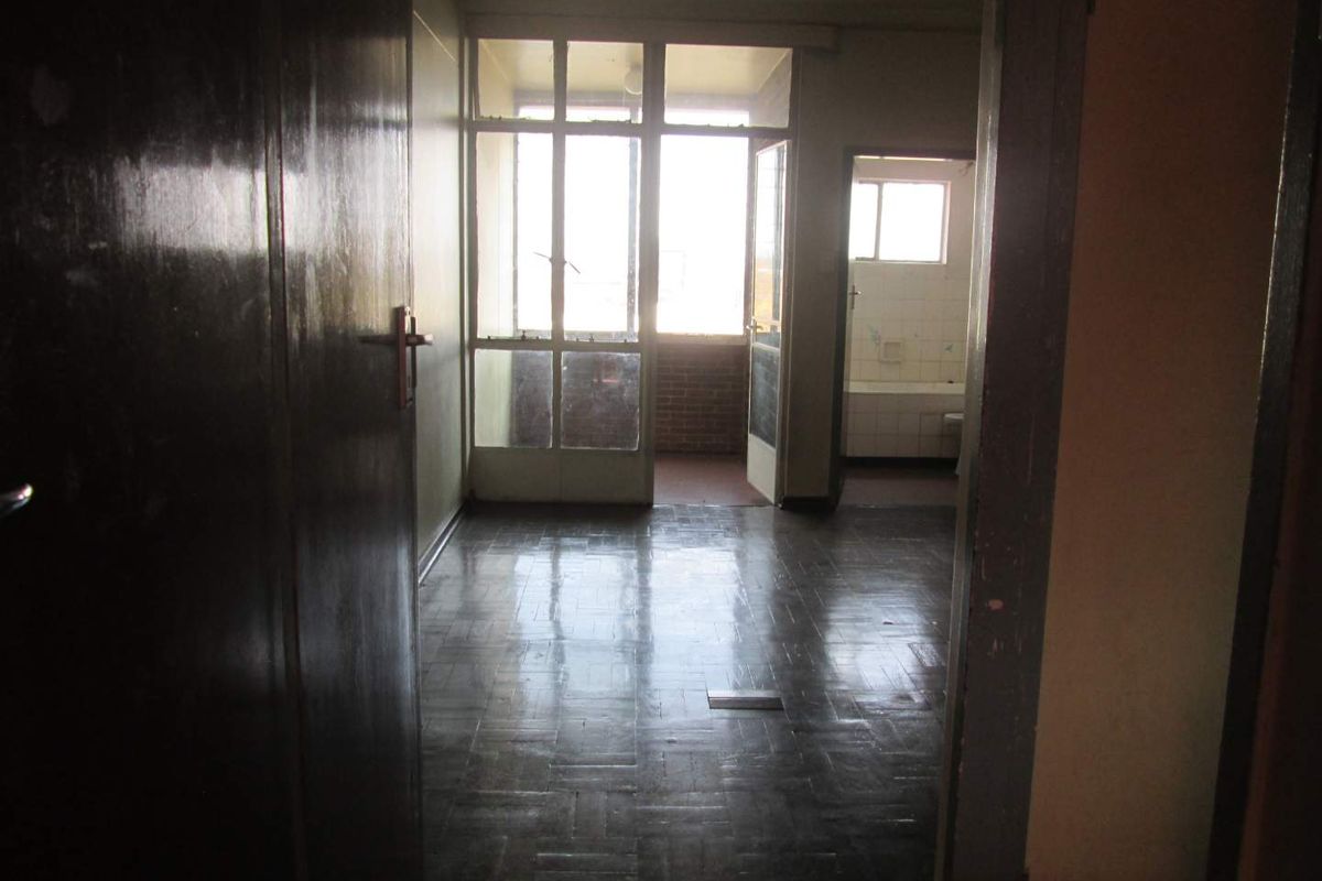 An empty living area featuring original parquet flooring and access to an adjoining balcony, showing signs of age and requiring cosmetic updates.