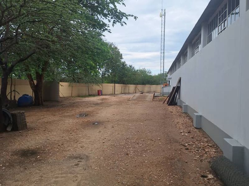Rear industrial yard area featuring a perimeter wall, communication tower, and an integrated weighbridge on an unpaved surface.