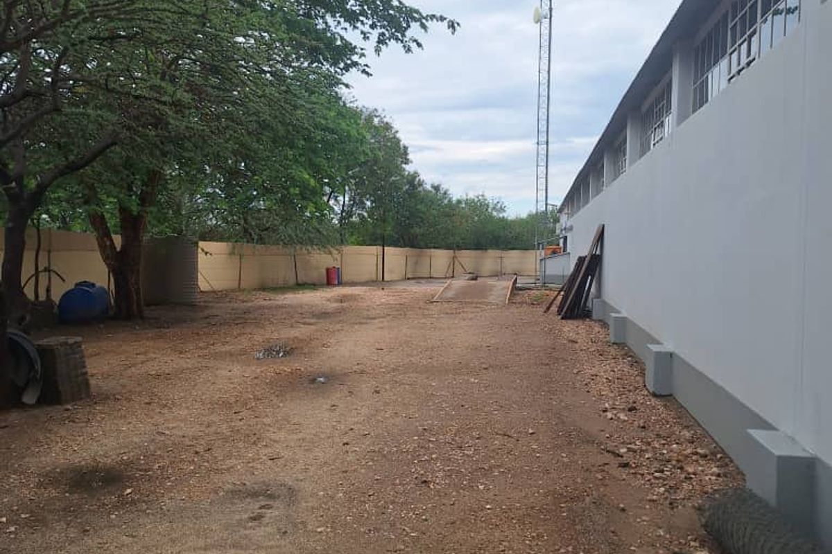 Rear industrial yard area featuring a perimeter wall, communication tower, and an integrated weighbridge on an unpaved surface.