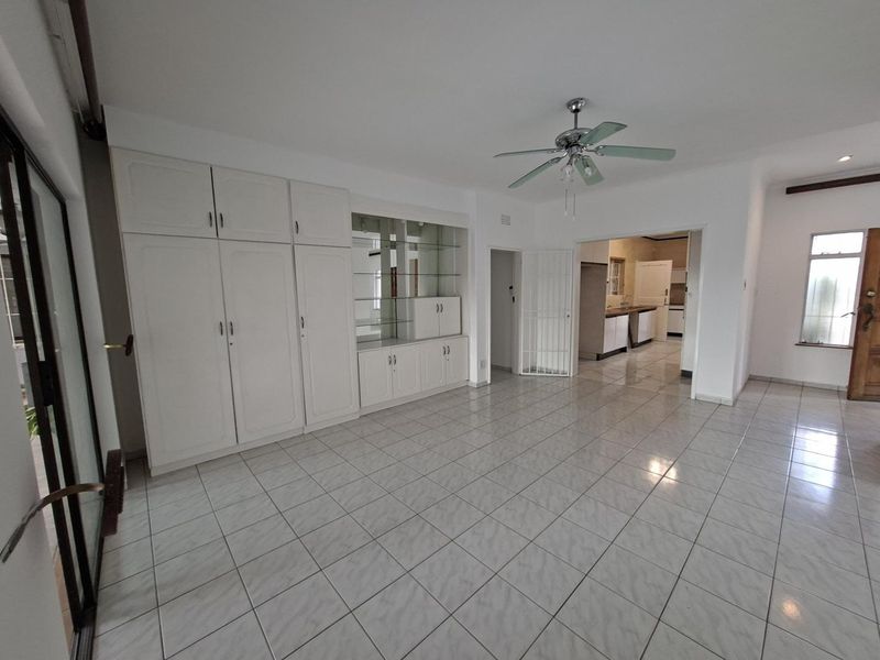 Spacious living area featuring neutral tiled flooring, built-in storage cabinetry, and a ceiling fan, with an open flow into the adjacent kitchen area.