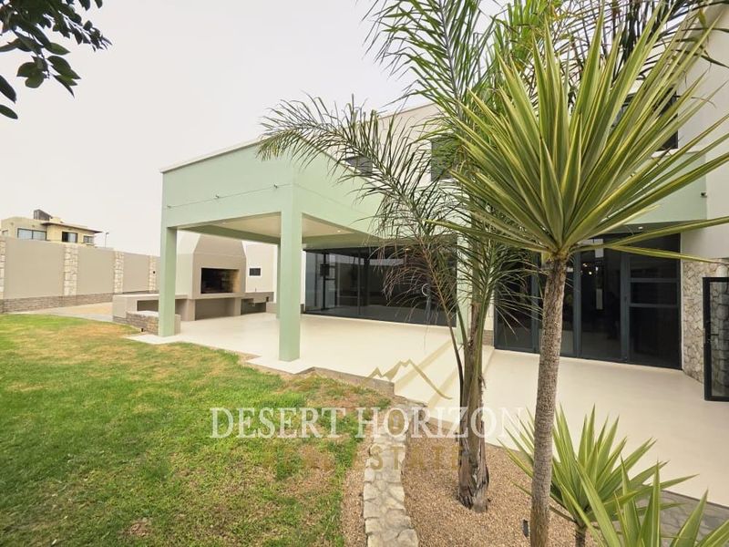 Spacious covered patio featuring a built-in braai, stone cladding accents, and large sliding glass doors providing seamless indoor-outdoor flow.