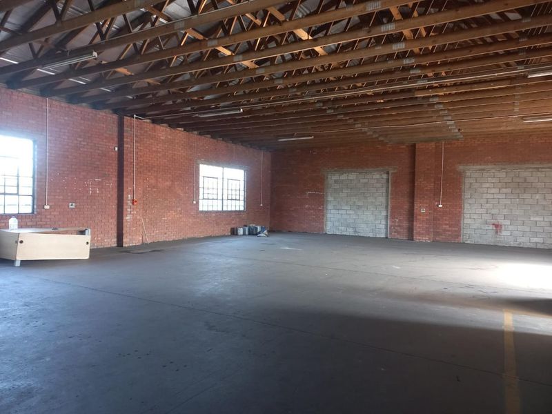 Spacious industrial warehouse unit featuring exposed timber roof trusses, brick walls, and durable concrete flooring with large steel-framed windows for natural light.