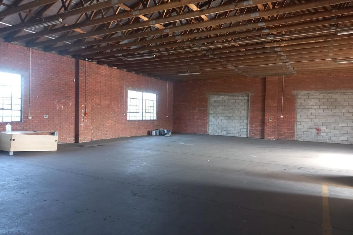 Spacious industrial warehouse unit featuring exposed timber roof trusses, brick walls, and durable concrete flooring with large steel-framed windows for natural light.