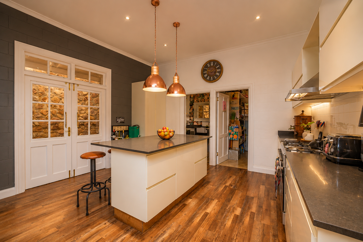 Modern kitchen featuring a central island with stone countertops, hardwood flooring, integrated appliances, and stylish pendant lighting, with access to a scullery area.