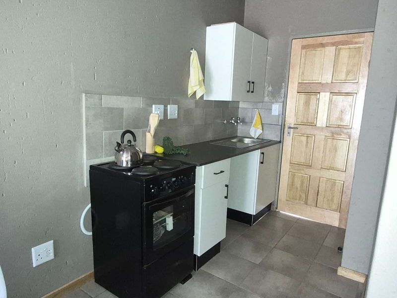 Compact kitchen area featuring built-in cabinetry, a stainless steel sink, tiled backsplash, and a freestanding stove with tiled flooring.