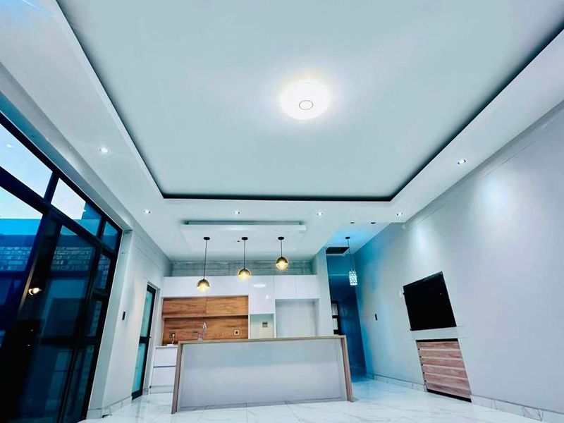 Modern open-plan living and kitchen area featuring sleek cabinetry, a central island, recessed lighting, and polished marble-look floor tiles.