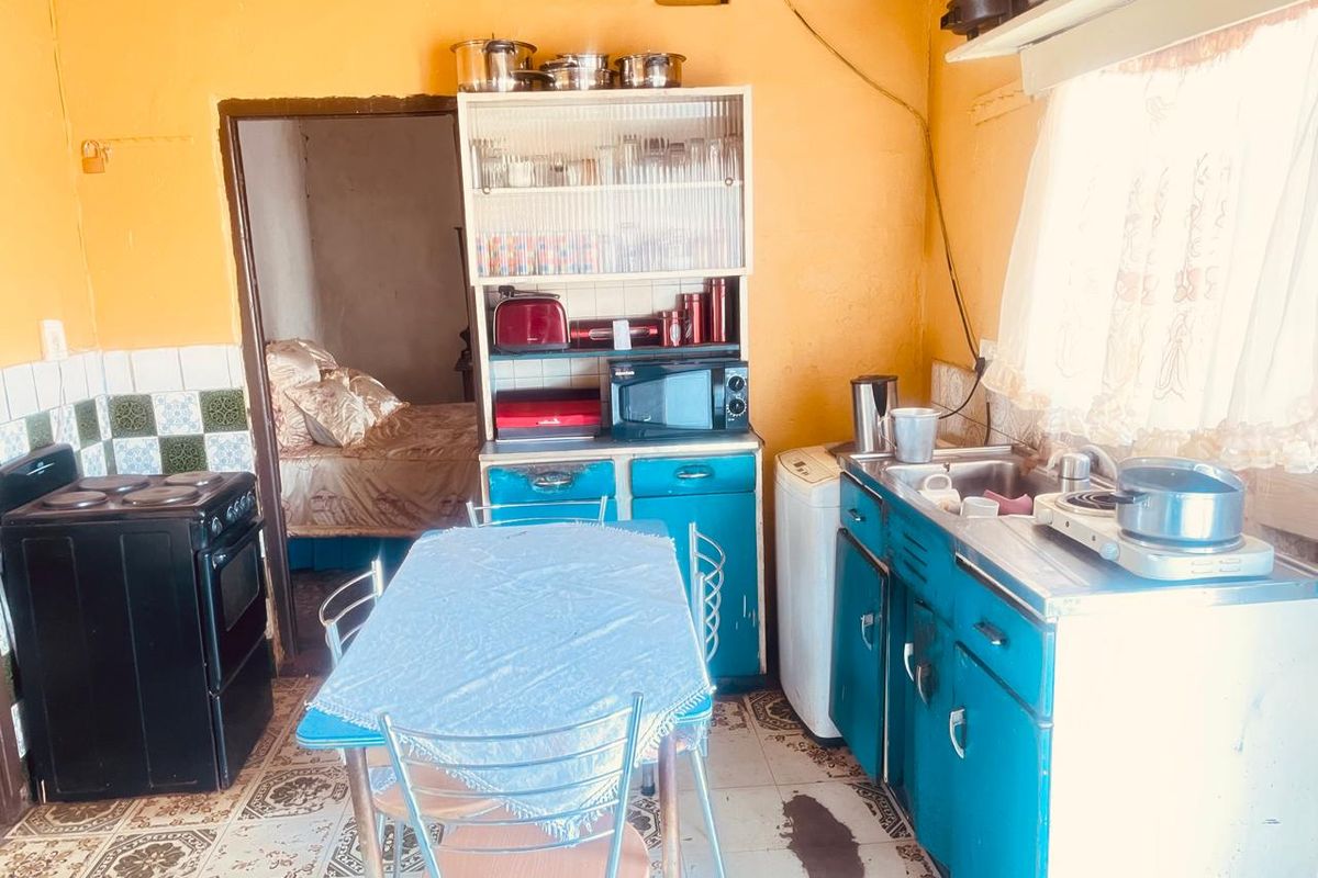 A dated kitchen featuring blue cabinetry, a stainless steel sink, patterned floor tiles, and a freestanding stove, requiring significant cosmetic updates.